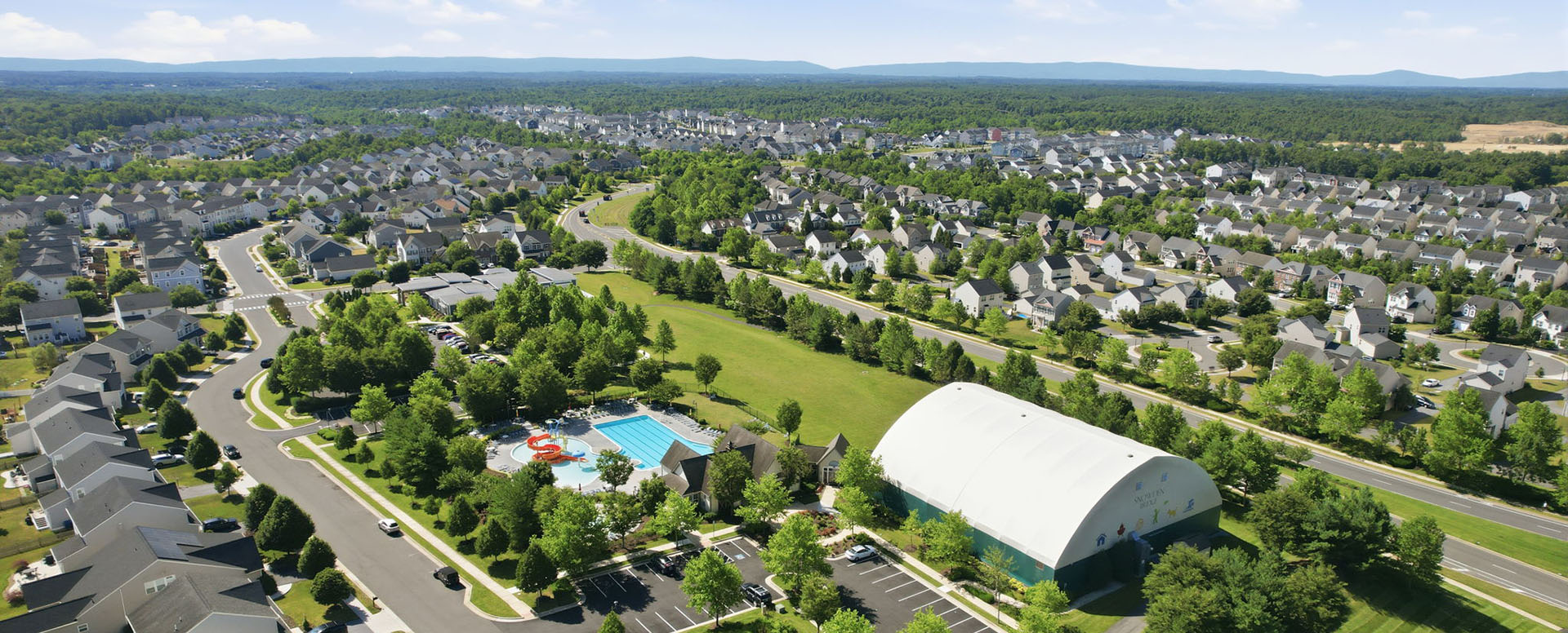 Aerial view of Snowden Bridge, a Brookfield master-planned community in Virginia, with homes stretching to the Blue Ridge and a community pool in the foreground